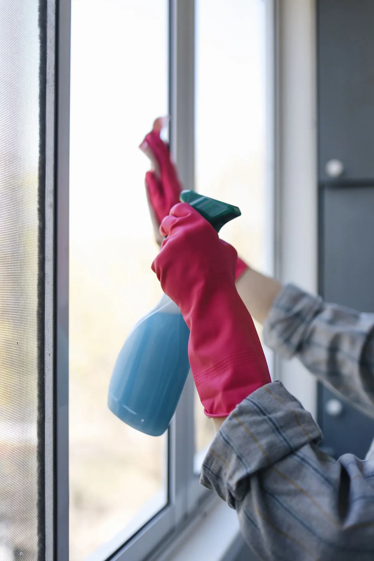 Gloved hands cleaning a window with a spray bottle